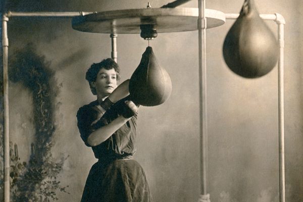 A young woman working out using boxing gloves and a punching bag in 1890.